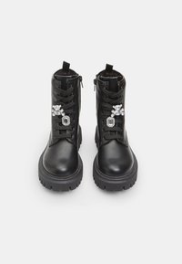 Botas de tobillo de cuero negro con punteras redondas, que cuentan con cordones en la parte delantera, cremalleras laterales y adornos de cristal en los laterales exteriores. Suelas resistentes.