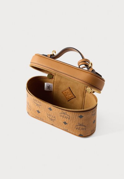 Sac en cuir marron clair avec logo MCM embossé, poignée supérieure, fermeture éclair dorée et compartiment intérieur doux avec petite étiquette logo.