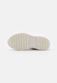 Bílá gumová podrážka tenisky s vroubkovaným vzorem, na kterém je ražený nápis "Converse". Hladký povrch, zaoblené hrany a plochý profil.