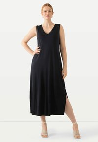 Abito lungo senza maniche di colore nero con scollatura a V, spacchi laterali e una superficie liscia. Abbinato a sandali beige con cinturini.