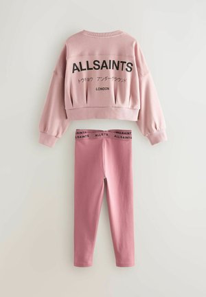 Felpa corta rosa con testo nero e loghi sul retro, abbinata a leggings rosa coordinati con vita nera.