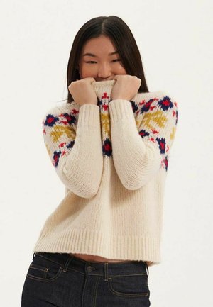 Pull en maille de couleur crème avec des motifs floraux multicolores sur les manches. Il présente un col montant, des poignets et un ourlet côtelés. Texture douce.