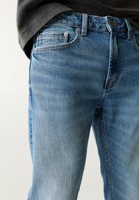 Lichtblauwe spijkerbroek van denim met een vervaagde textuur, vijf zakken ontwerp en gestikte details langs de naden en tailleband.