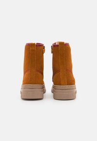 Suede ankle boots in orange with a contrasting red interior and stitching; features a chunky beige sole and a short zipper at the back.
