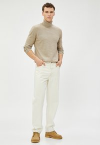 Beige Rollkragenpullover aus Baumwollmix; weiße gerade Jeans mit sichtbaren Nähten; braune Stiefel. Schlichtes Design, entspannte Passform.