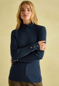 Námornícky modrá rebrovaná blúzka s dlhým rukávom, riaseným stojacím golierom a gombíkovými detailami na rukávoch, vyrobená z mäkkej látky. Minimalistický dizajn.