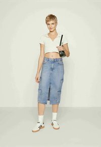 Saias midi em denim azul claro com uma fenda frontal, bolsos aplicados e cintura ajustada. Usada com um top branco cropped e sapatilhas.