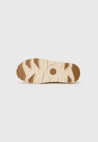 Lichtgekleurde sneakerzool met een gestructureerd ontwerp; bevat diepe loopvlakken, een cirkelvormig embleem in het midden en bruine accenten.