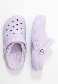 Zoccoli Crocs lavanda con fori di ventilazione e imbottitura in fleece, mostrati in vedute dall'alto e di lato su uno sfondo bianco.