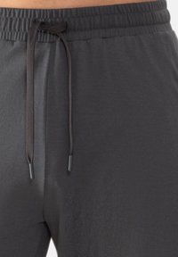 Donkergrijze joggingbroek met een elastische tailleband, voorzien van een bruine trekkoord en zwarte plastic uiteinden. Glad, iets glanzend stofoppervlak.