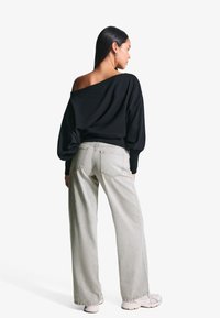 Fekete, vállról lelógó pulóver ballon ujjakkal, világosszürke, széles szárú nadrággal és bézs sportcipővel párosítva. Sima textúra és laza szabás.