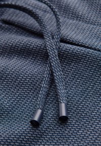 Twee blauwe, gestructureerde stoffen koordjes met plastic uiteinden die op een bijpassende, gestructureerde blauwe stof liggen.