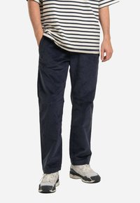 Navy corduroy trousers with a relaxed fit. Features side pockets and a straight leg design, paired with a striped short-sleeve shirt and sneakers.