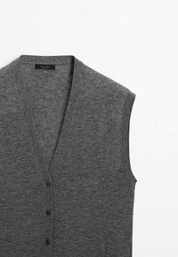 Gilet en maille sans manches gris foncé avec col en V et trois boutons noirs sur le devant, posé à plat sur un fond blanc.