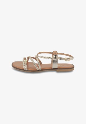 Metallic silver flat sandal with braided straps and a buckled ankle strap, featuring a tan sole and minimalistic design.