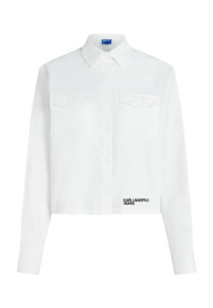 Baltas ilgomis rankovėmis trumpintas marškinėlis su sagomis priekyje, dviem sagotu krūtinės kišenėmis, smailiu apykakliu ir „KARL LAGERFELD JEANS“ logotipu netoli apačios.