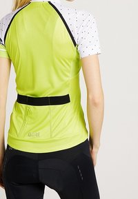 Jersey de ciclismo verde con mangas cortas de lunares blancos, y un bolsillo trasero. Cintura negra y logo reflectante de "GORE" en la parte inferior.