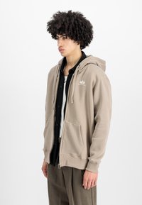 Sudadera con capucha en mezcla de algodón marrón claro, con cremallera frontal, dos bolsillos y un pequeño logotipo blanco en el lado izquierdo del pecho.