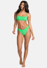 Bikini set verde brillante a costine composto da un top corto con spalline sottili e culotte a vita alta, entrambi realizzati in tessuto elasticizzato.