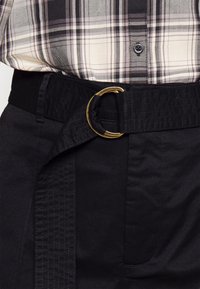 Czarne spodnie z szerokim pasem i złotą okrągłą klamrą. Posiadają teksturę w podszewce i boczne kieszenie, w zestawie z koszulą w kratę.