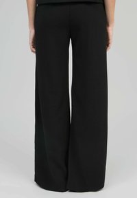 Pantalons noir à jambes larges en tissu doux et lisse. Présente une taille haute et un drapé subtil, sans matériel ou motifs visibles.