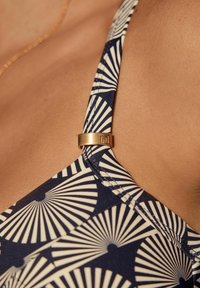 Marinblå bikiniöverdel med vitt fläktmönster, prydd med en guldfärgad metallaccent på remmen, som har en mjuk och stretchig tygtextur.