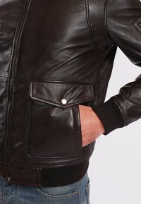 Black leather bomber jacket featuring front zipper, two chest pockets with flaps, ribbed cuffs, and a smooth, glossy texture.