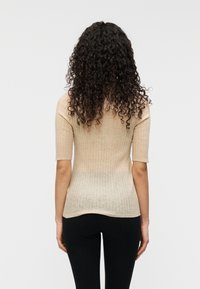 Μπεζ ριμπ πλε κτό τοπ με κοντά μανίκια, εφαρμοστό σιλουέτα και διακριτή υφή, σε συνδυασμό με μαύρο παντελόνι, από πίσω όψη.