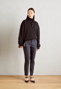Černá oversized polo košile s límečkem a knoflíky, spojená s tmavými upnutými kalhotami a černými lodičkami s špičatou špičkou a dekorativními kotníkovými pásky.
