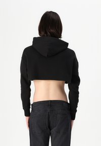 Black cropped hoodie with a hood, featuring long sleeves. Worn with dark denim jeans, showcasing a fitted silhouette and bare midriff.