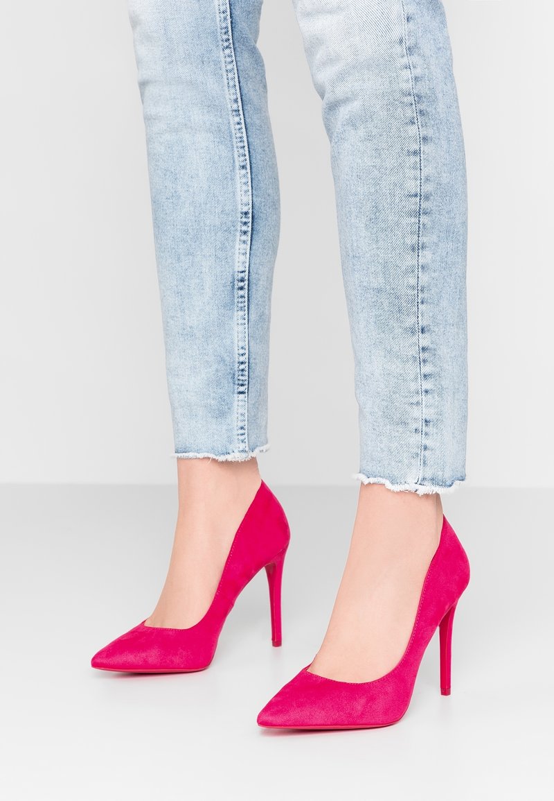 Escarpins en suède rose avec un bout pointu et un talon aiguille. Ce modèle présente un décolleté bas et une texture lisse. Portés avec un jean délavé.