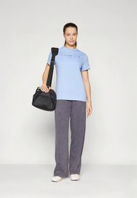 Hele sinine puuvillane t-särk "Champion" logoga, kombineeritud hallide laia säärega pükstega. Modell hoiab musta riidest käekotti, millel on reguleeritav rihm.