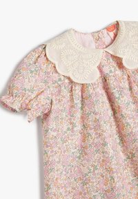 Bloemenjurk met een crèmekleurige gegolfde kraag. Heeft roze, oranje en groene bloemenpatronen op een lichte stof. Puffmouwen en een geraffineerde taille.
