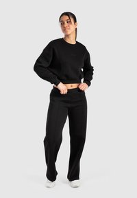 Sweatshirt noir court avec des coutures ton sur ton et un col rond, associé à un pantalon de survêtement noir taille haute, le tout en tissu doux.
