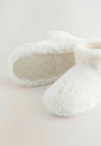 Pehmeate, kohevate valgete susside paar, millel on tekstureeritud, libisemiskindlad taldad heledal taustal.