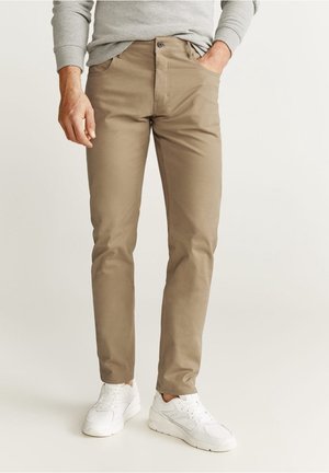 Miesten vaaleanbeiget chinos-housut, joissa on slim fit -lahkeet, valmistettu sileästä kankaasta. Housuissa on etutaskut, napitus ja ne on yhdistetty valkoisiin tennareihin.