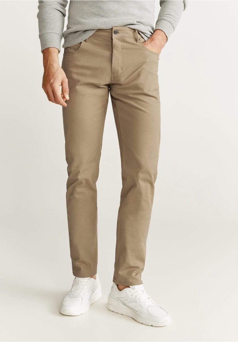 Beige chino's voor mannen met een slim fit, gemaakt van een gladde stof. Voorzien van voorzakken, een knoopsluiting en gedragen met witte sneakers.