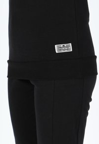Black cotton sweatshirt with ribbed cuffs and hem. Features a small white label with "DENIM FACTORY" text. Close-up view of fabric texture.