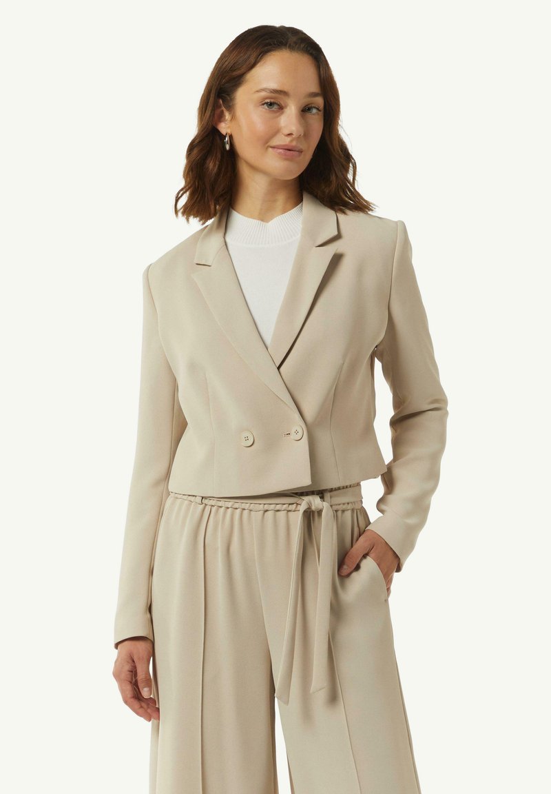 Beige dubbele-breasted blazer met notch-revers, zachte stof en een cropped ontwerp, gecombineerd met bijpassende hooggerokte broek met een strikriem.