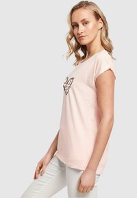 Lys rosa afslappet t-shirt med opsmøgede korte ærmer, som har et sort leopardprint hjerte design på fronten. Blød bomuldsstruktur.