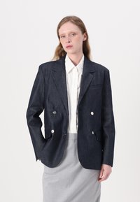 Sacou bleumarin din denim, cu două rânduri de nasturi argintii, revere cu tăietură, și două buzunare frontale; asortat cu o cămașă albă cu nasturi.