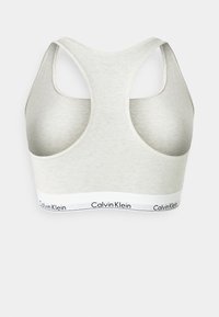 Lys grå sports BH med racerback-design, laget av mykt stoff. Har et kontrasterende hvitt bånd med "Calvin Klein"-logo.