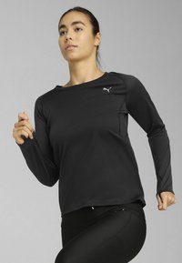 Camiseta atlética de manga larga negra con escote redondeado, corte ajustado y detalle sutil del logo. La tela parece suave y transpirable.
