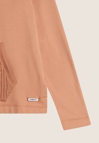 Maglietta a maniche lunghe color pesca realizzata in tessuto morbido, con tasca a coste, etichetta con logo e design aderente con cuciture pulite.