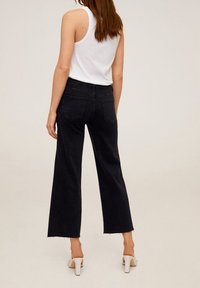 Schwarze Jeans mit weitem Bein aus Denim, mit hoher Taille, zwei Gesäßtaschen und rohem Saum. Kombiniert mit hellfarbigen High-Heels.