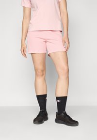 T-shirt rose côtelé associé à un short rose assorti. Porté avec des chaussures de sport noires et des chaussettes noires avec un logo.
