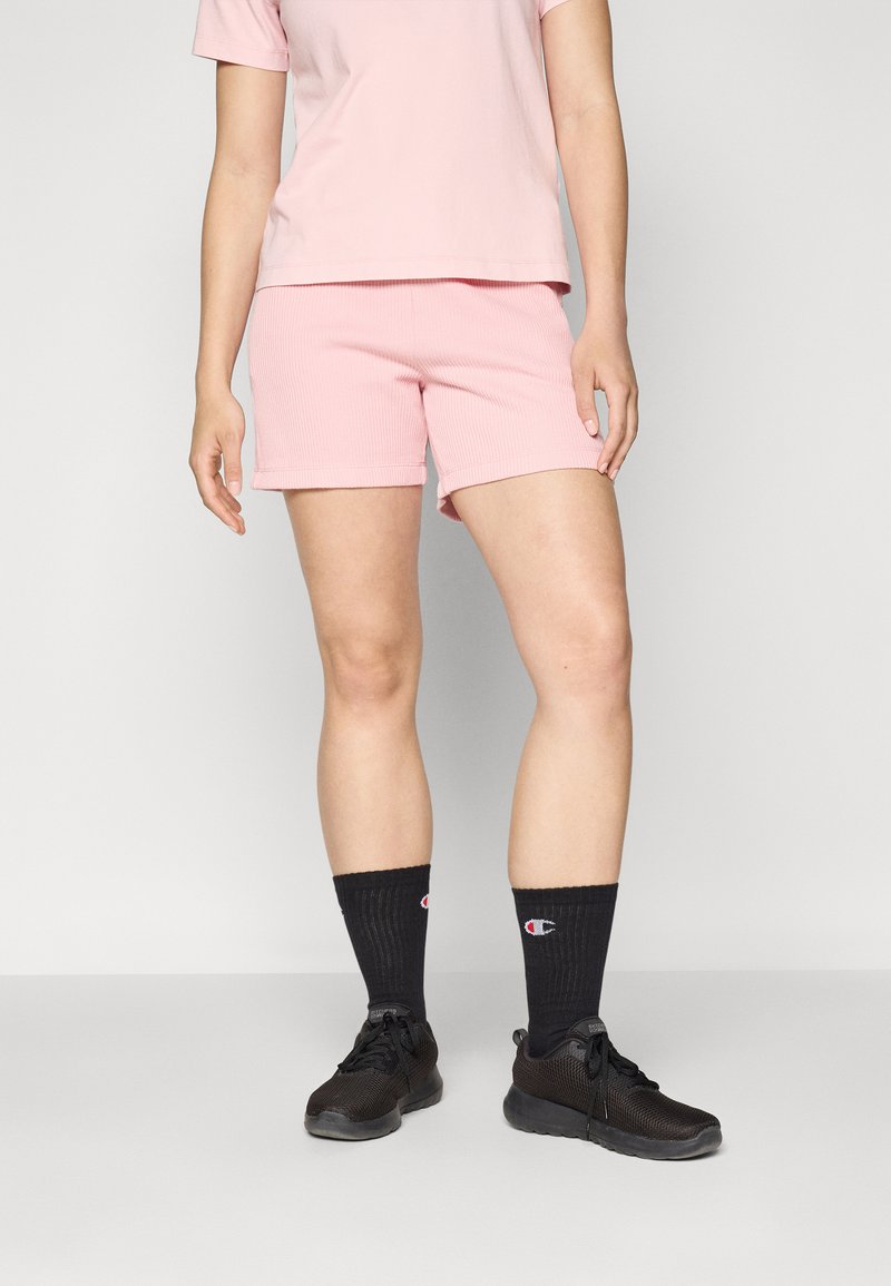 T-shirt rose côtelé associé à un short rose assorti. Porté avec des chaussures de sport noires et des chaussettes noires avec un logo.