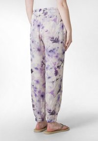 Lätta byxor med blommönster i pastelllila och krämfärg; har elastisk midja och draperade ärmslut; tillsammans med platta sandaler.