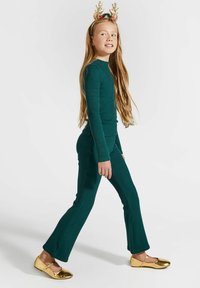 Zielony, prążkowany zestaw do noszenia w domu, składający się z bluzki z długim rękawem i rozszerzanych spodni, zestawiony z błyszczącymi, złotymi butami typu Mary Jane oraz świąteczną opaską z porożem.