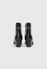 Bottes de cheville en cuir noir avec un talon arrondi, présentant une fermeture éclair à l'arrière et un accent doré avec un détail de logo.